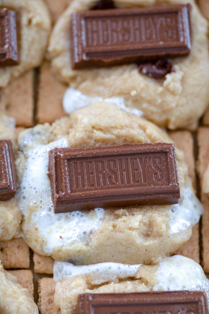 S'mores cookie bars half baked on baking sheet with Hershey's chocolate piece pressed in center of cookies