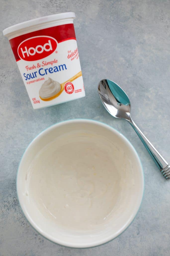 Bird's eye view of sour cream container, spoon, and bowl with white caesar dressing