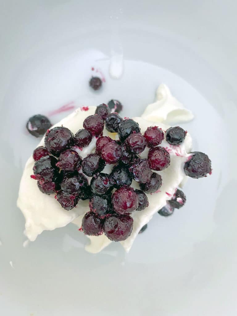 Sour cream icing with frozen blueberries on top in bowl.