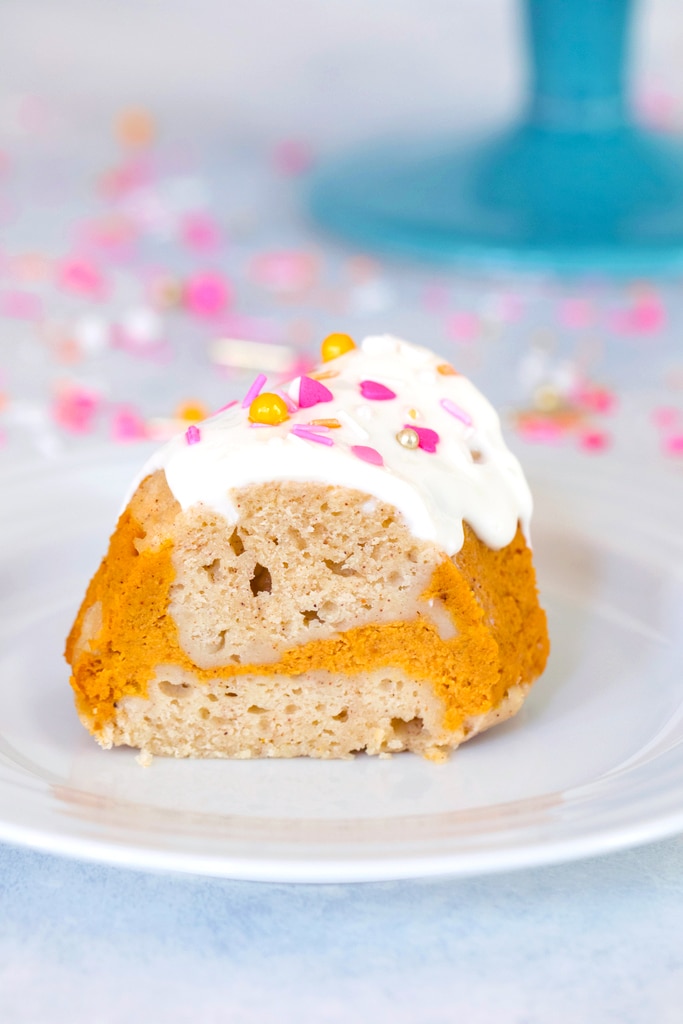 Head-on view of a slice of sour cream pumpkin pie bundt cake with pumpkin swirl and pink and orange sprinkles on a white plate with sprinkles in the background