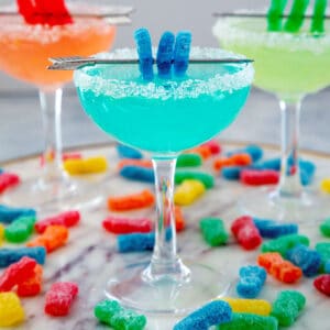 Head-on view of blue Sour Patch Kids margarita with two more cocktails in background and candies all around