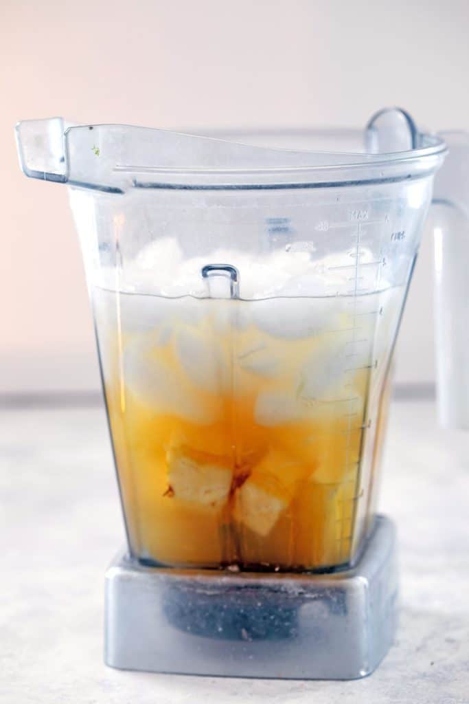 Head-on view of blender with pineapple, pineapple juice, ice and more for cocktail