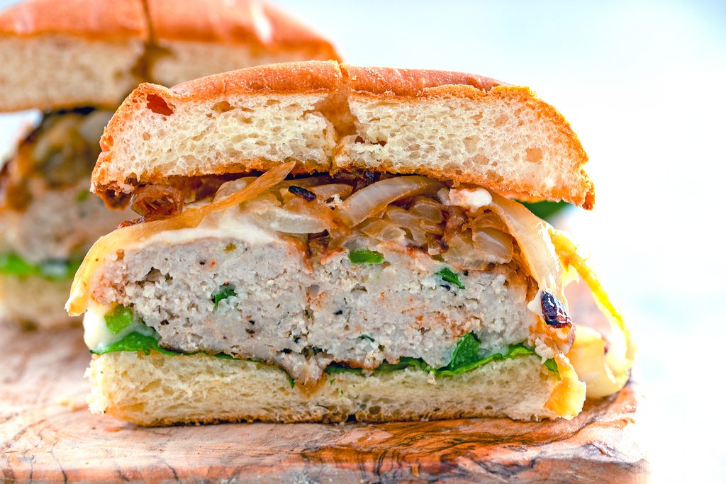 Landscape view of a spicy cheesy chicken burger with caramelized onions cut in half on wooden cutting board