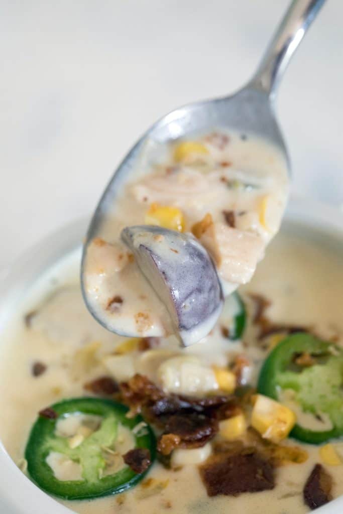 A spoonful of spicy clam chowder with corn, potatoes, and clams being held over a bowl