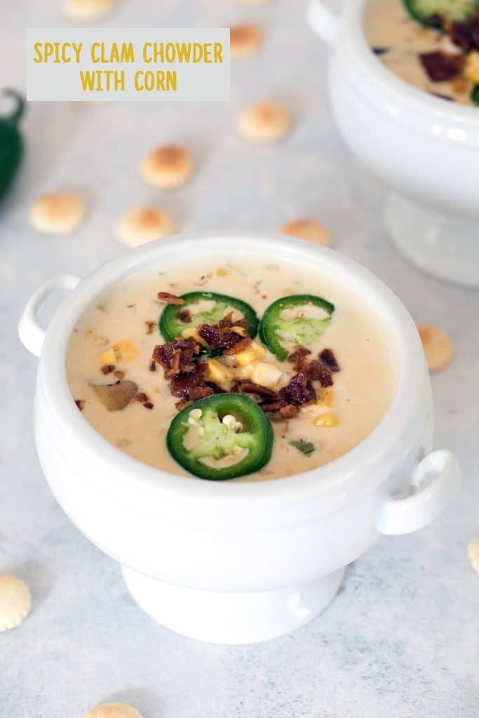 Overhead view of a white bowl of spicy clam chowder with corn topped with bacon and jalapeños and surrounded by oyster crackers with recipe title at top