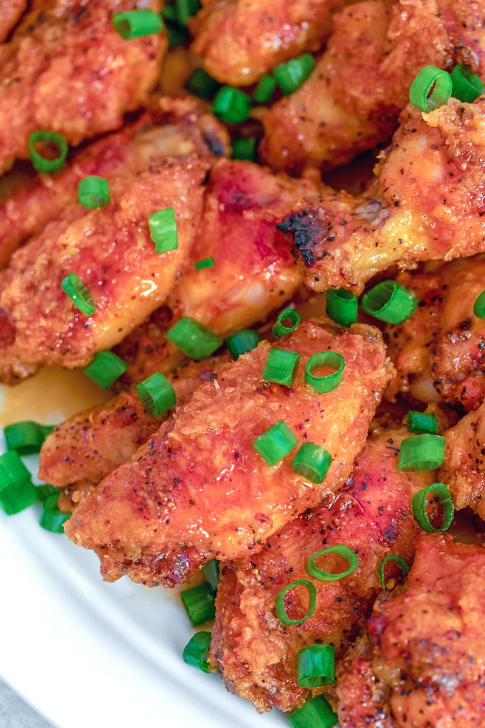 Overhead close-up version of spicy ginger honey wings piled up on a platter and scattered with scallions