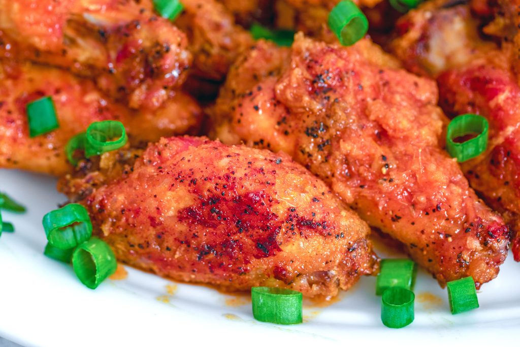 Landscape closeup view of a couple spicy ginger honey wings surrounded by more wings and chopped scallions on a white platter