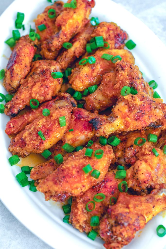 Bird's eye view of a white platter stacked with spicy ginger honey chicken wings with chopped scallions everywhere