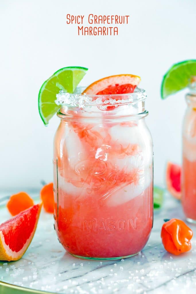 Head-on view of a spicy grapefruit margarita in a mason jar with lime and grapefruit garnish and recipe name at top of image