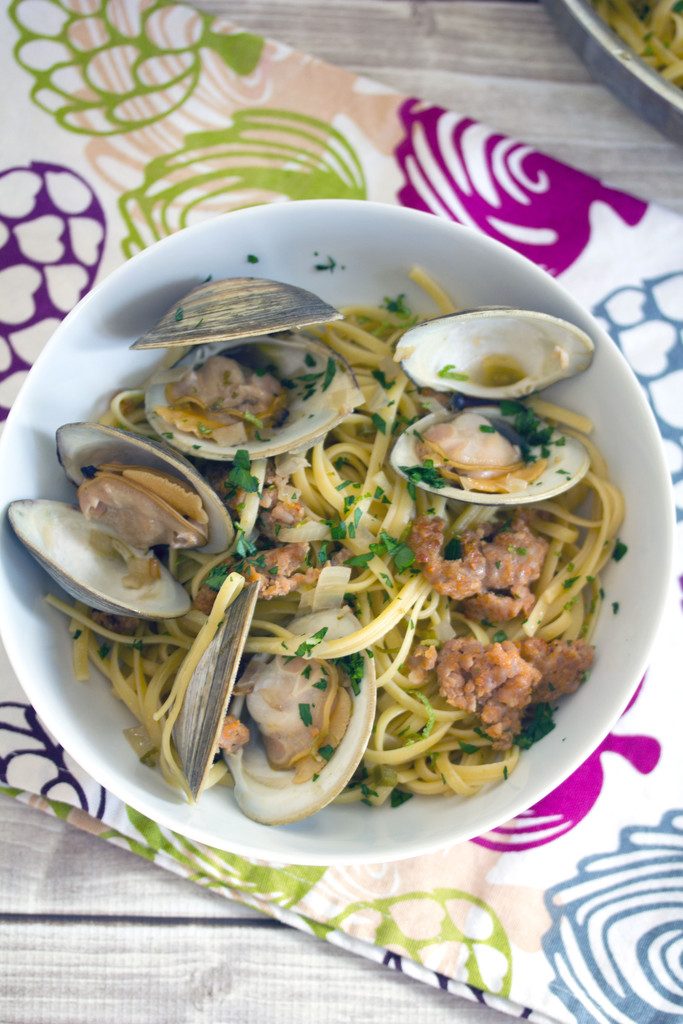 Bird's eye view of a white bowl of spicy lime linguine with clams and sausage on a colorful tea towel