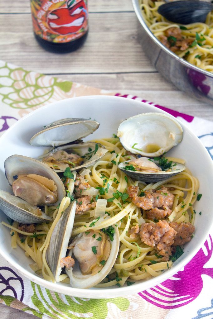 Overhead view of a big bowl of spicy lime linguine with clams and sausage with a hard cider in the background