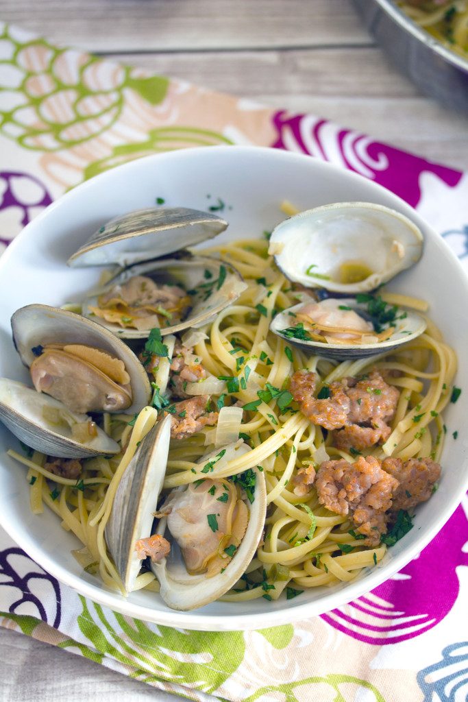 Overhead view of a white bowl of spicy lime linguine with clams and sausage, topped with parsley