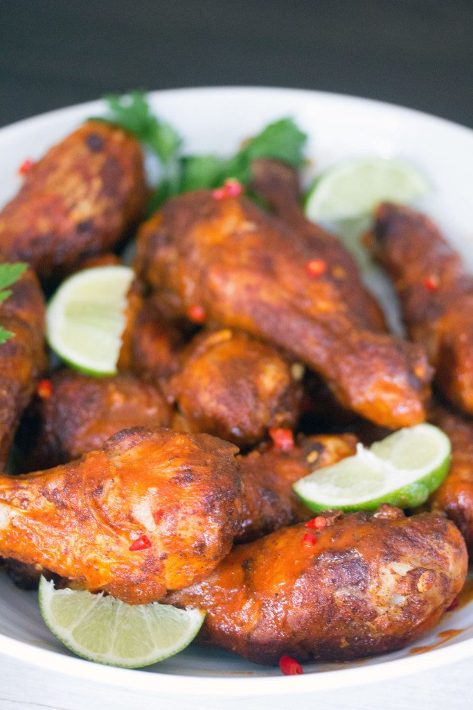 Head-on view of a white serving bowl filled with Spicy Thai Chicken Drumsticks with lime wedges and parsley