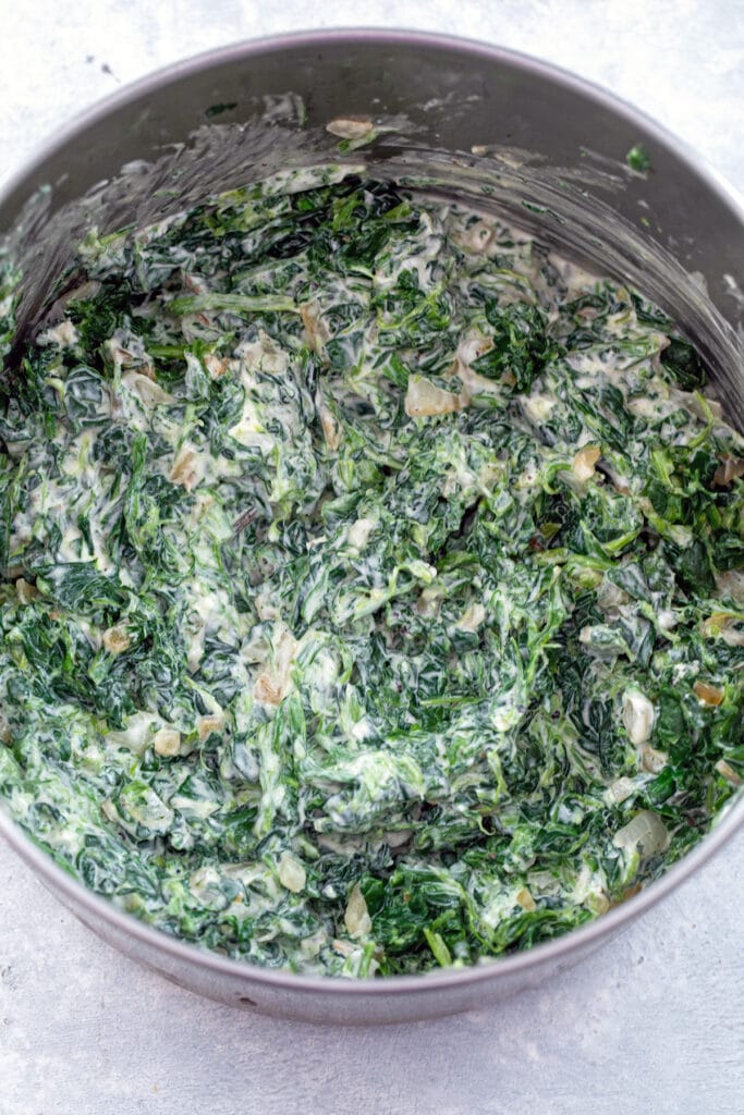 Spinach being mixed with cream cheese in saucepan