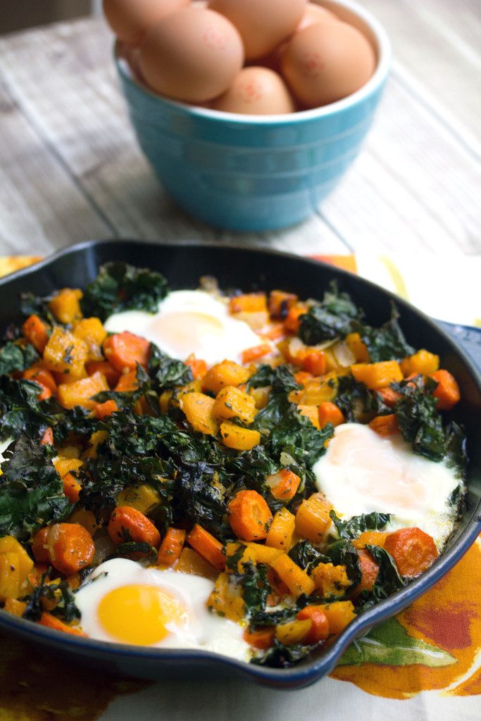 Overhead view of squash hash with kale and eggs in a cast iron skillet with bowl of eggs in the background