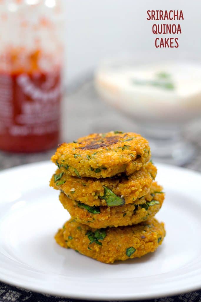 Head-on closeup view of four sriracha quinoa cakes stacked on each other on a white plate with a bottle of sriracha and yogurt dipping sauce in the background with recipe name at the top
