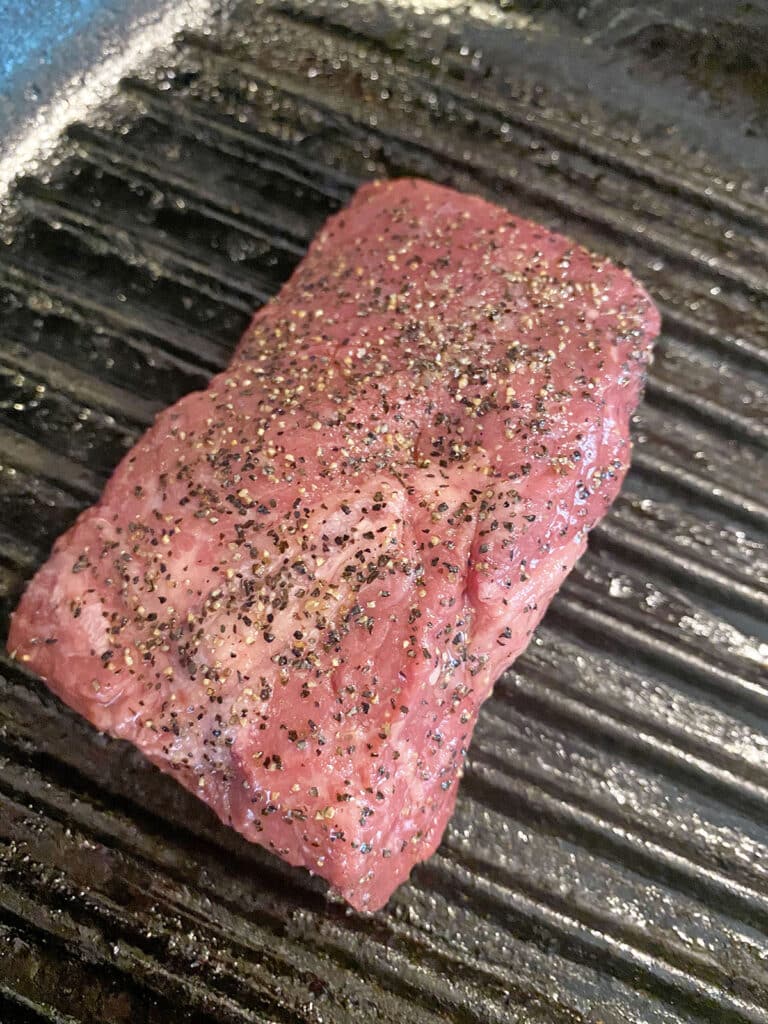 Sirloin steak with salt and pepper cooking in grill pan.