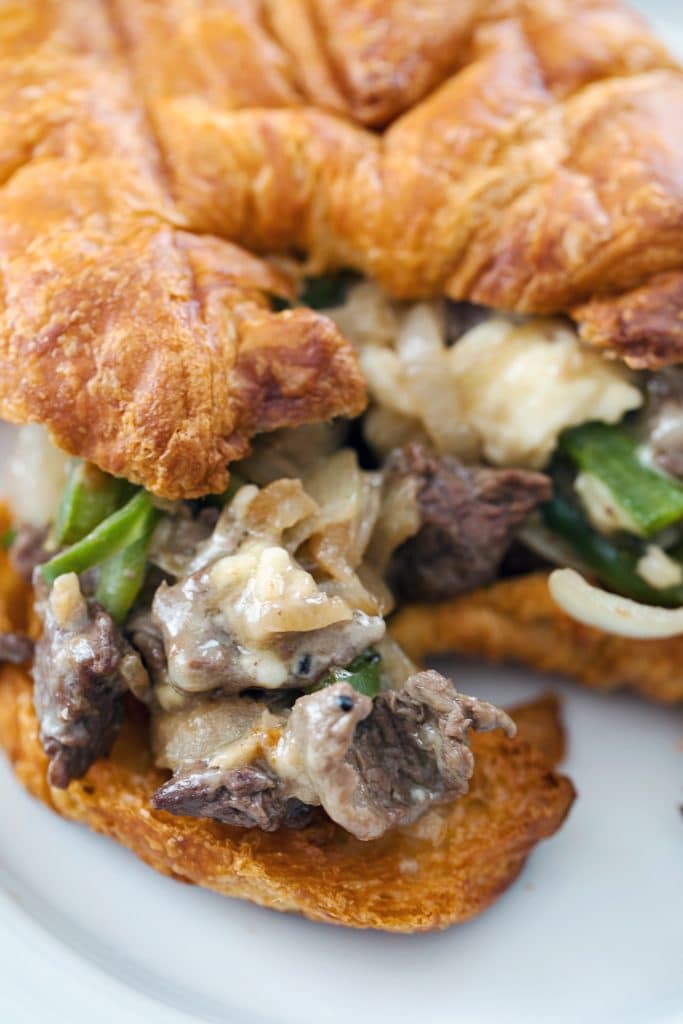 Close-up of steak and cheese croissant with steak, white cheese, green peppers, and onions
