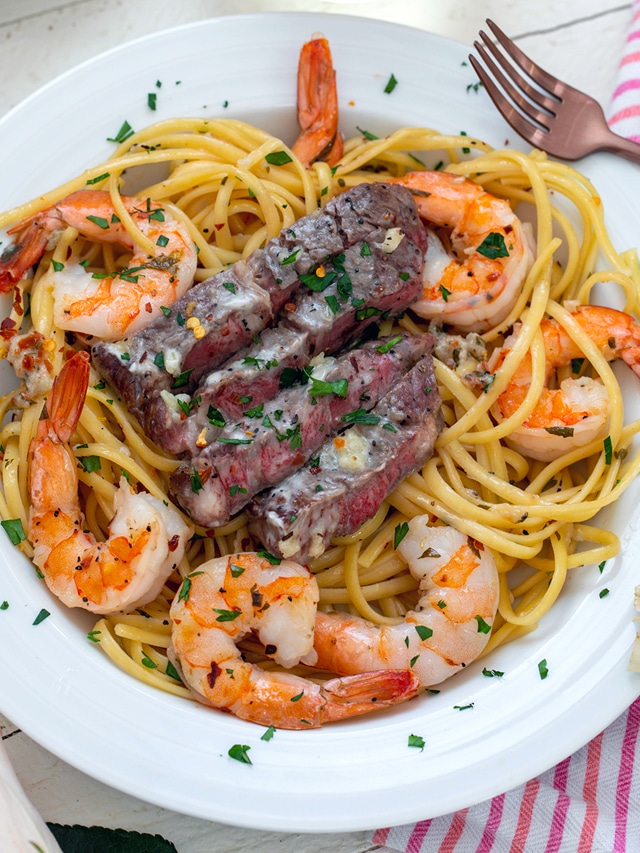 Overhead closeup view of steak and shrimp pasta in a white bowl.