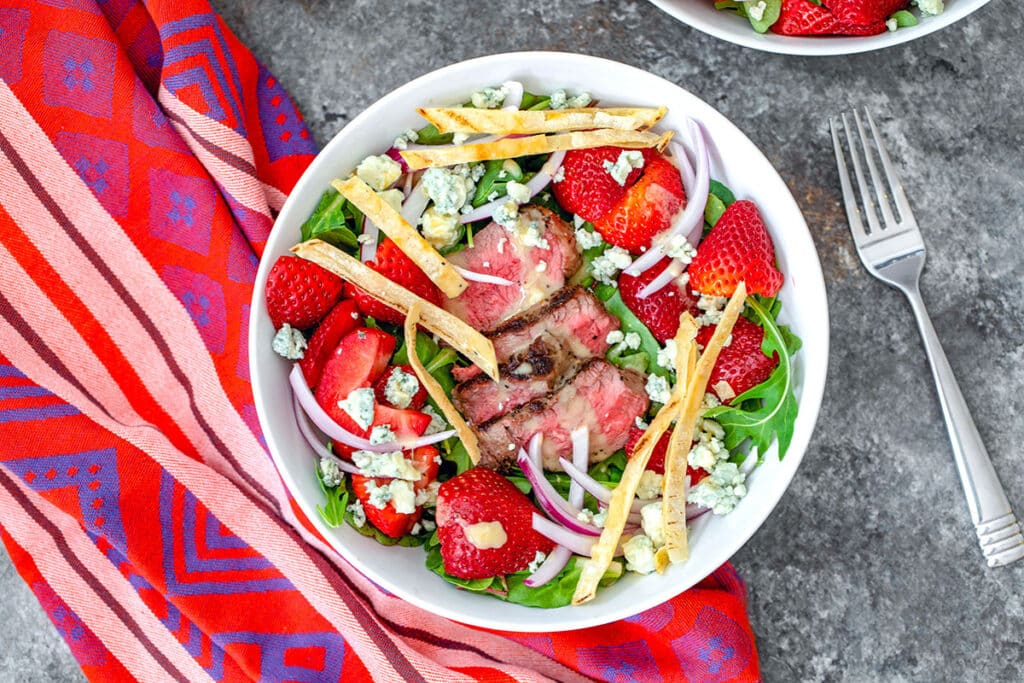 Landscape view of steak and strawberry salad in white bowl with fork next to it.