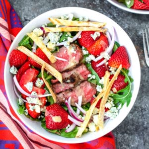 Closeup view of a steak strawberry salad with tortilla strips and blue cheese.