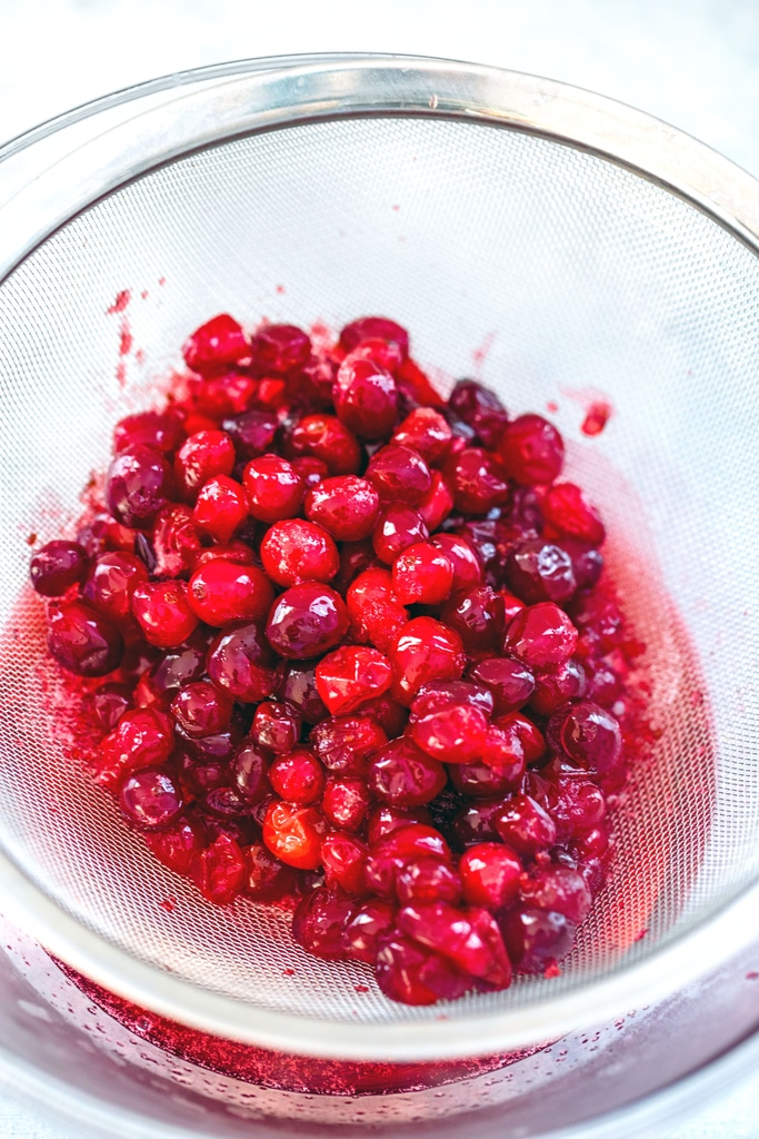 Cranberries in strainer over bowl to extract juice
