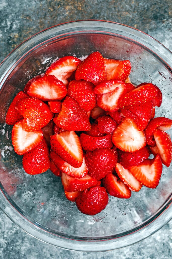 Overhead view of glass bowl of sliced strawberries with sugar