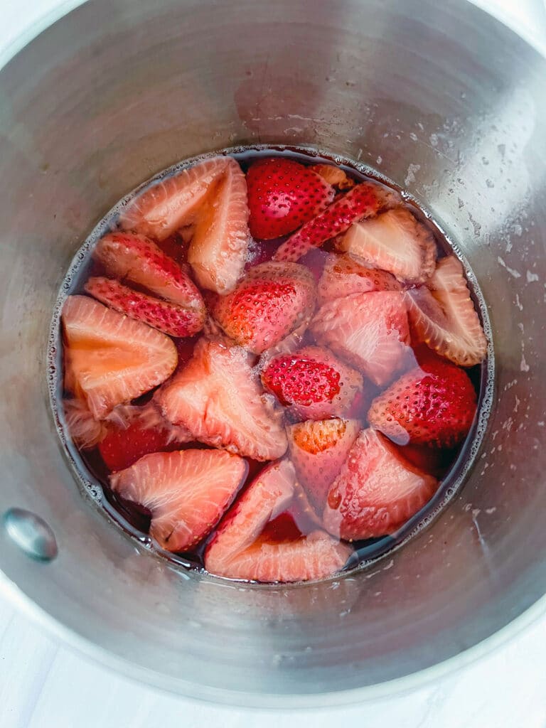 Strawberries simmered in white grape juice in saucepan.