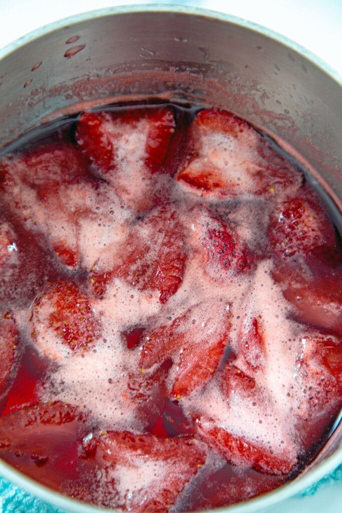 Sliced strawberries simmering with water in sugar in saucepan.