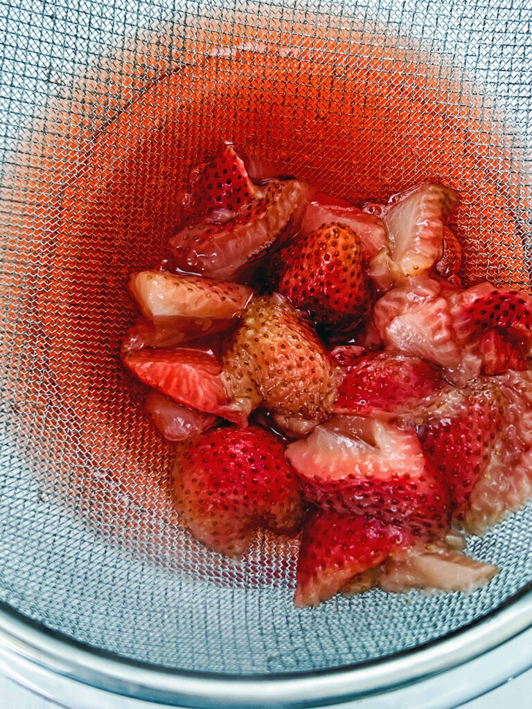 Strawberries being strained out of white grape juice.