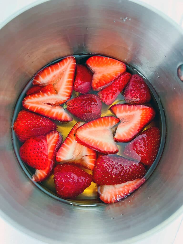 Overhead view of sliced strawberries in white grape juice in saucepan.