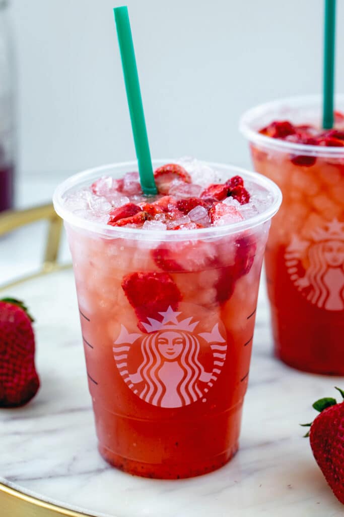 Head-on view of a strawberry acai refresher in a Starbucks cup with ice and freeze-dried strawberries.
