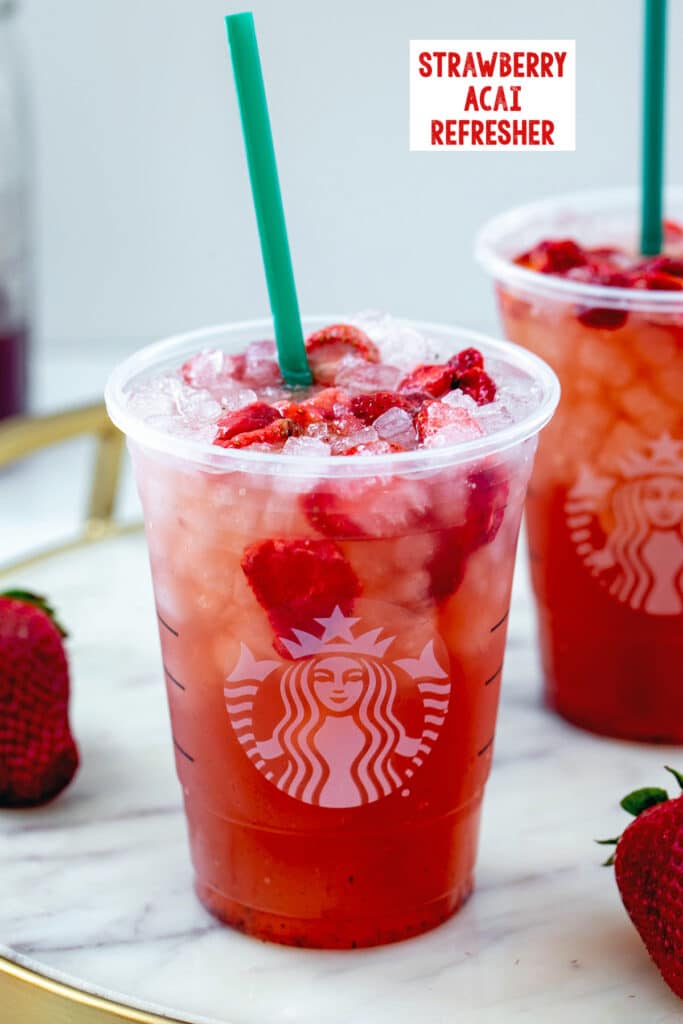 Head-on view of a strawberry acai refresher in a Starbucks cup with ice and freeze-dried strawberries with recipe title at top.