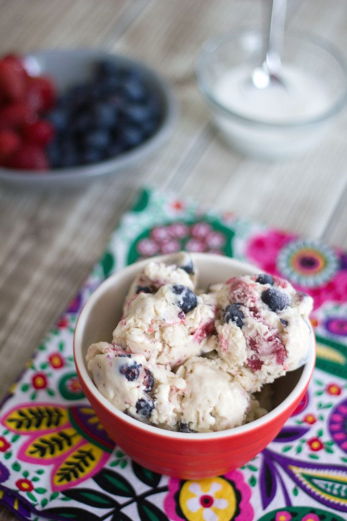 Overhead view of bowl of strawberry blueberry ice cream on colorful placemat with bowl of strawberries and blueberries and bowl of marshmallow fluff in background