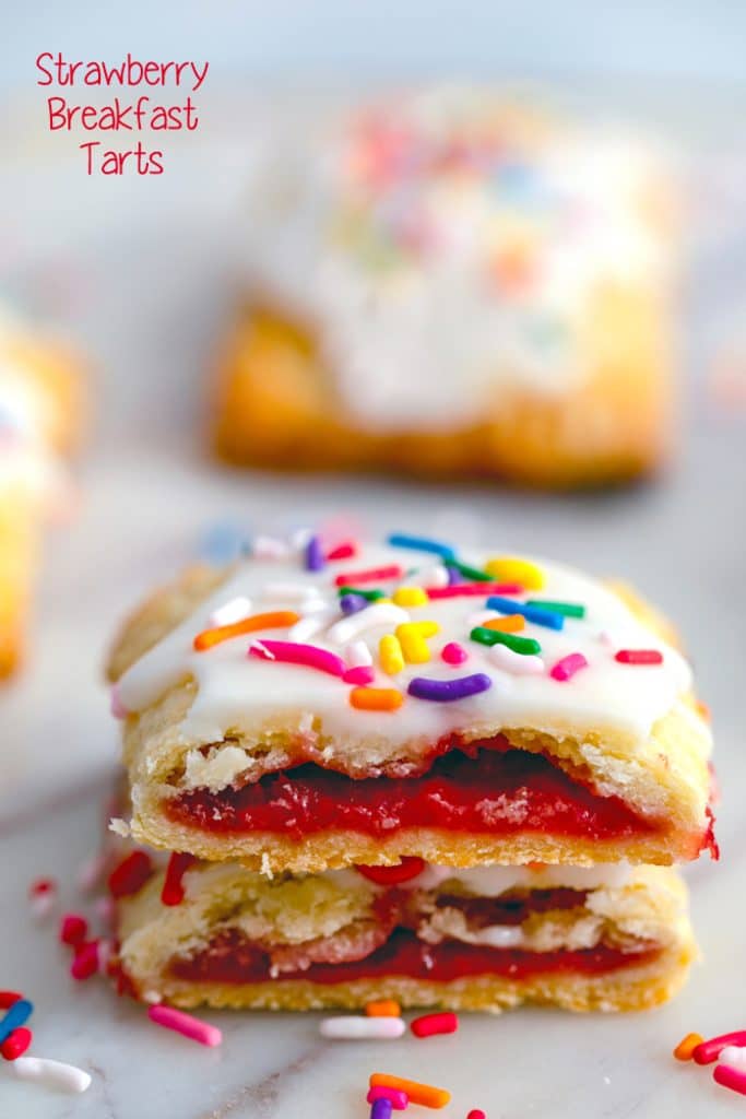 Two halves of strawberry breakfast tart stacked on top of each other with strawberry jam oozing out and icing and sprinkles on top with "Strawberry Breakfast Tarts" text at the top