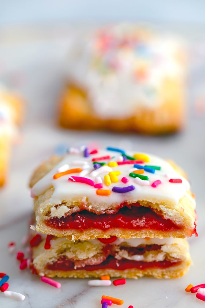 Two halves of strawberry breakfast tart stacked on top of each other with strawberry jam oozing out and icing and sprinkles on top