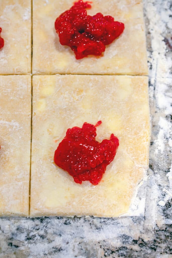 Rectangle of dough cut into four with strawberry jam on top.