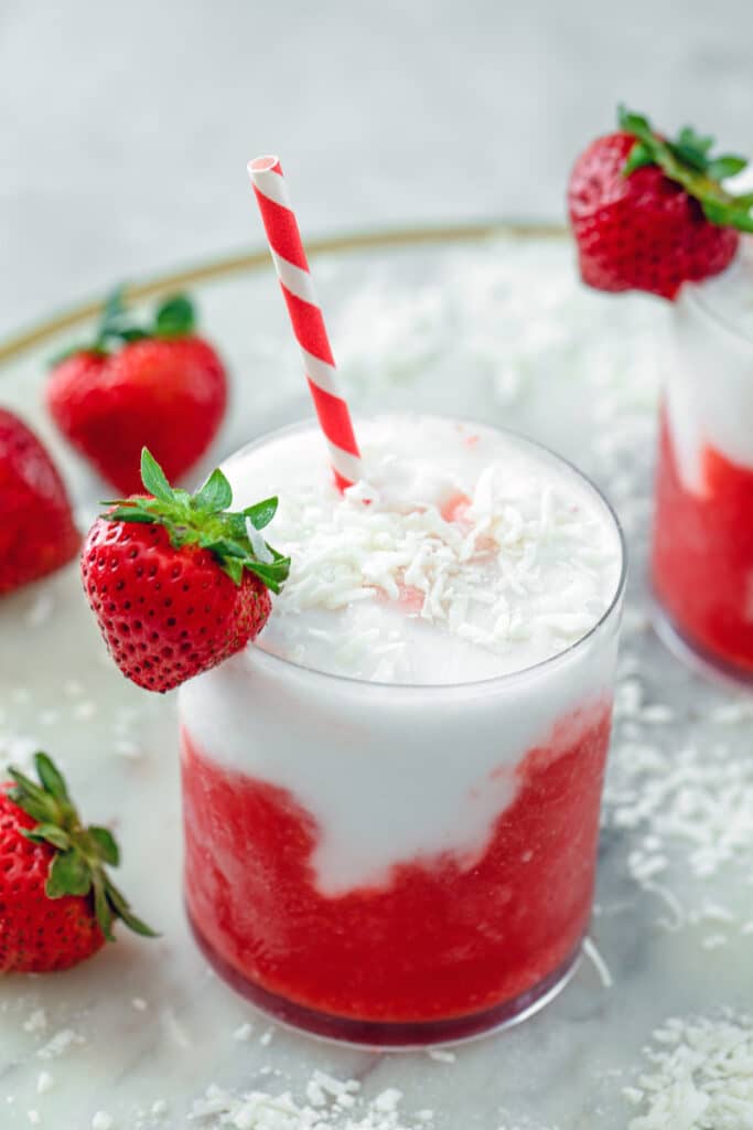 Overhead view of a strawberry coconut daiquiri with shredded coconut and strawberry garnish and red and white straw