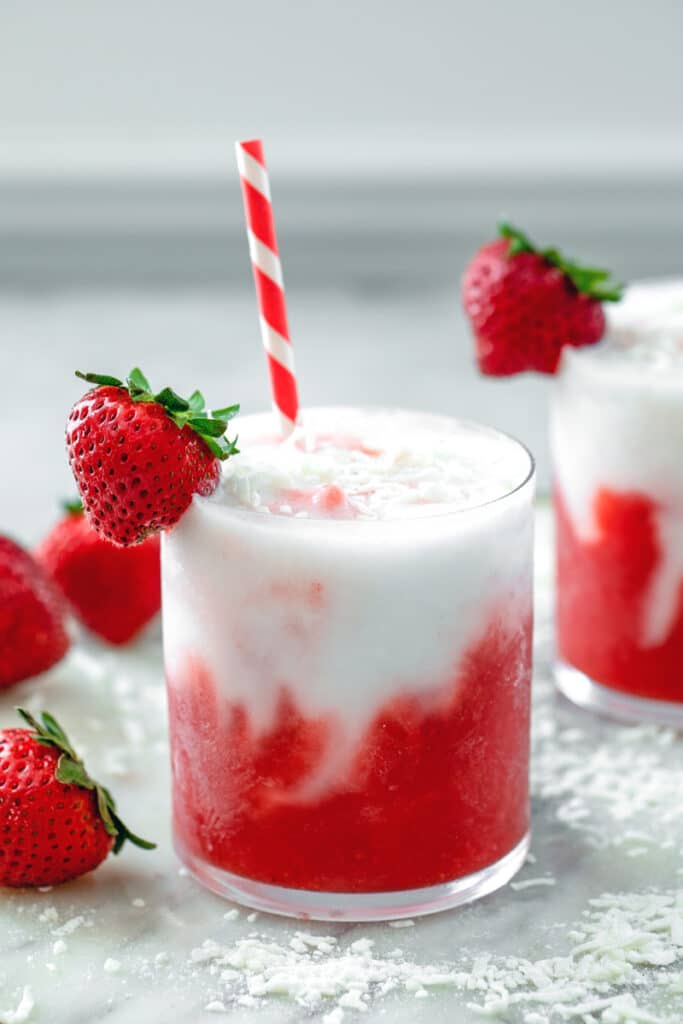 Head-on closeup view of a red and white strawberry coconut daiquiri with shredded coconut and strawberries on top and all around