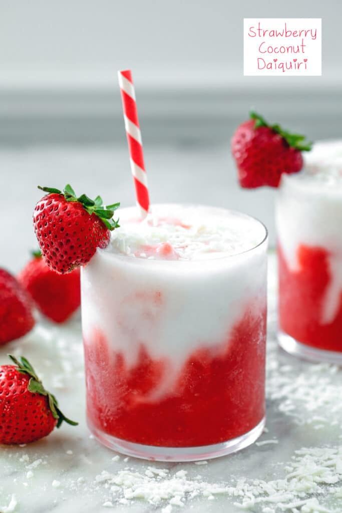 Head-on closeup view of a red and white strawberry coconut daiquiri with shredded coconut and strawberries on top and all around and recipe title at top