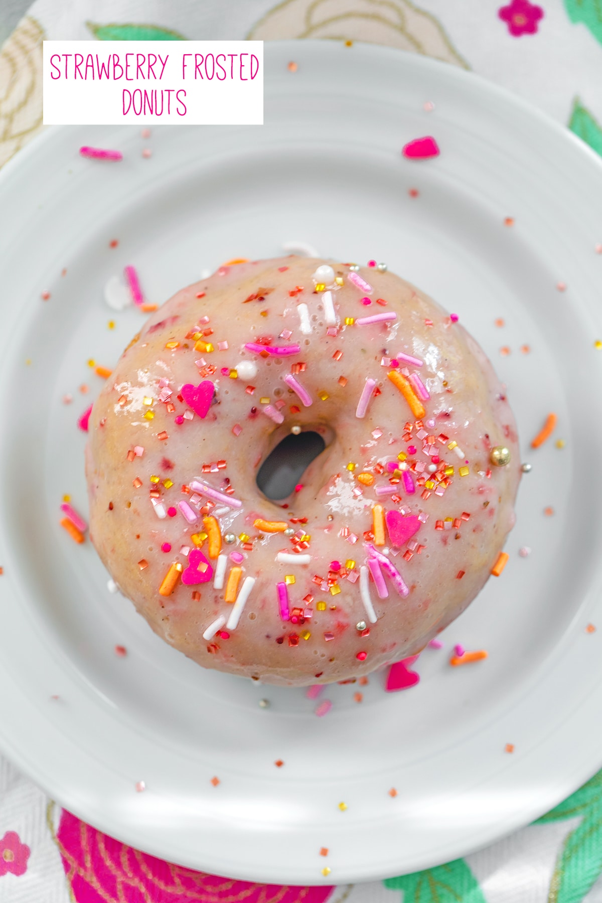 Overhead view of a Strawberry frosted donut covered in pink sprinkles on a white plate with recipe title at top.