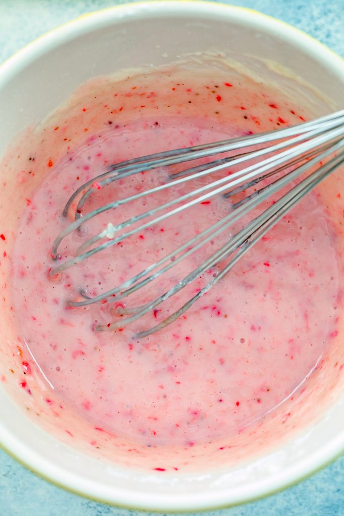 Overhead view of pink strawberry icing in mixing bowl with whisk