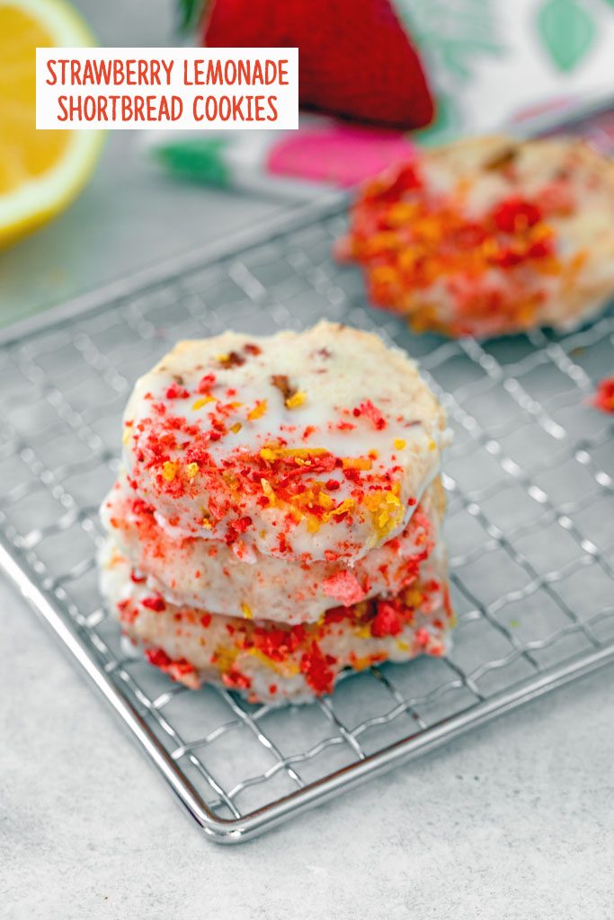 Overhead view of a stack of strawberry lemonade shortbread cookies on a metal rack with more cookies, a lemon half, and a strawberry in the background with recipe title at top