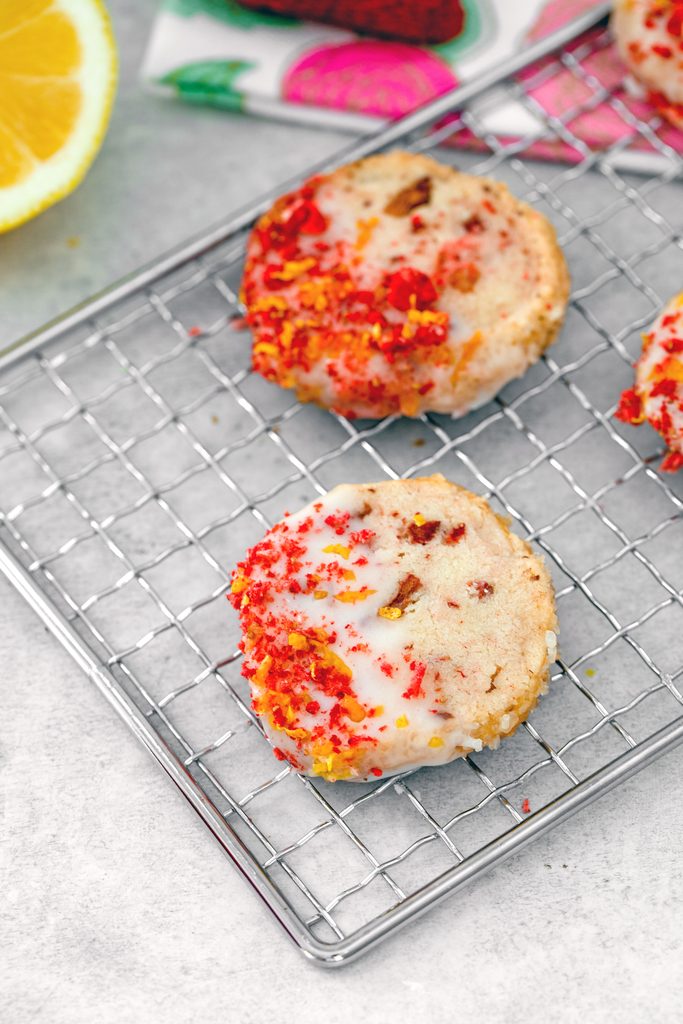 Bird's eye view of strawberry lemonade shortbread cookies on metal baking rack with half a lemon in the background