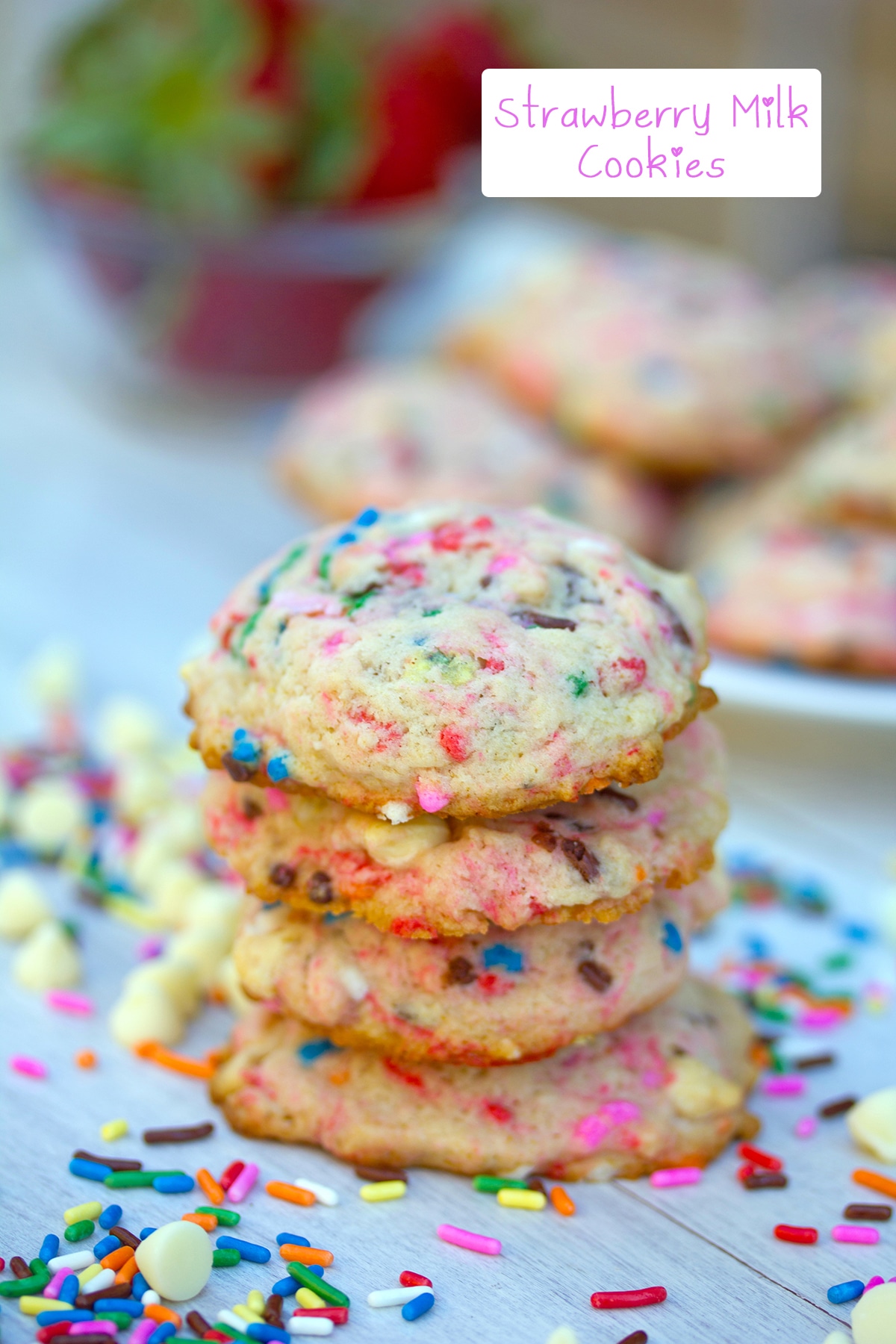 Stack of strawberry milk cookies with rainbow sprinkles and white chocolate chips all around and recipe title at top.