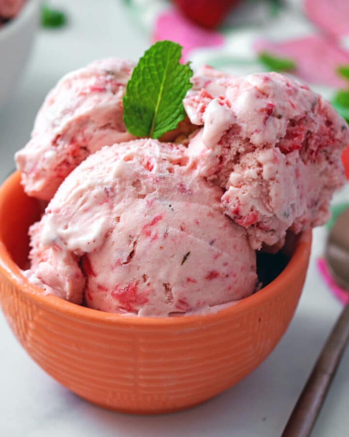Head-on closeup view of strawberry mint ice cream in a bowl with a rose gold spoon on the side