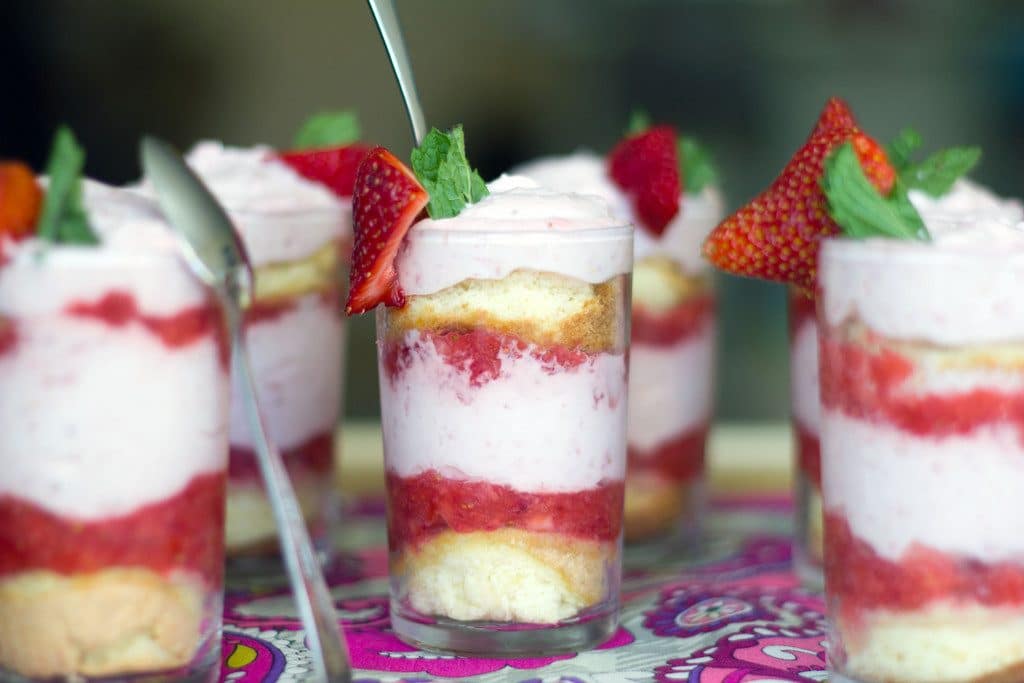 Landscape view of several strawberry mousse parfaits all lined up with sponge cake, strawberry purèe, and strawberry mousse