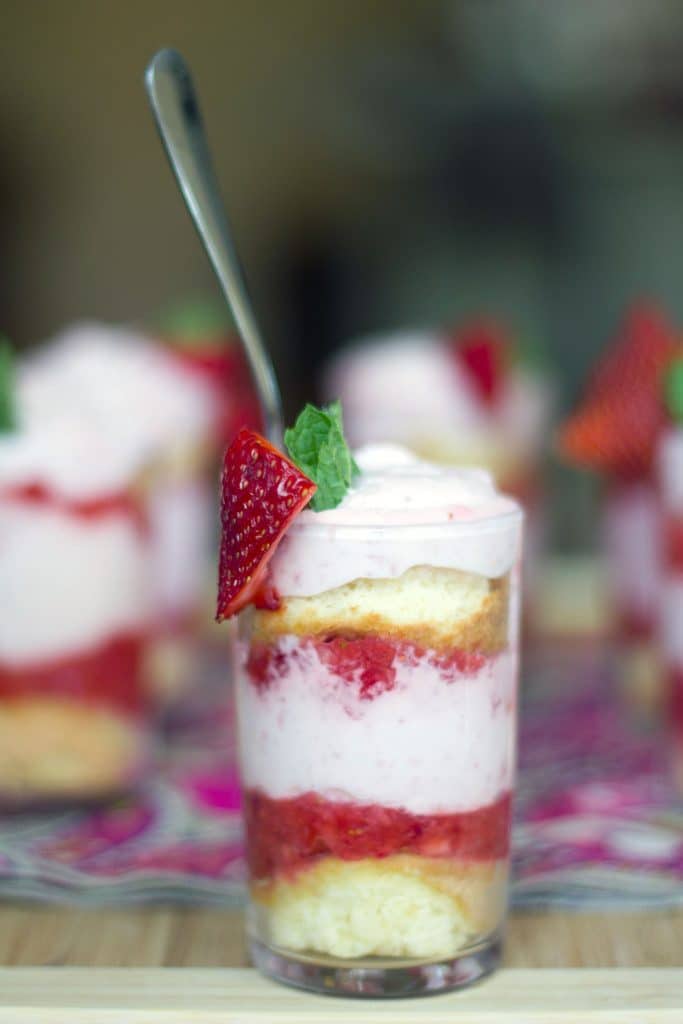 Head-on view of a mini strawberry mousse parfait with sponge cake, strawberry purée and strawberry mousse with more parfaits in background