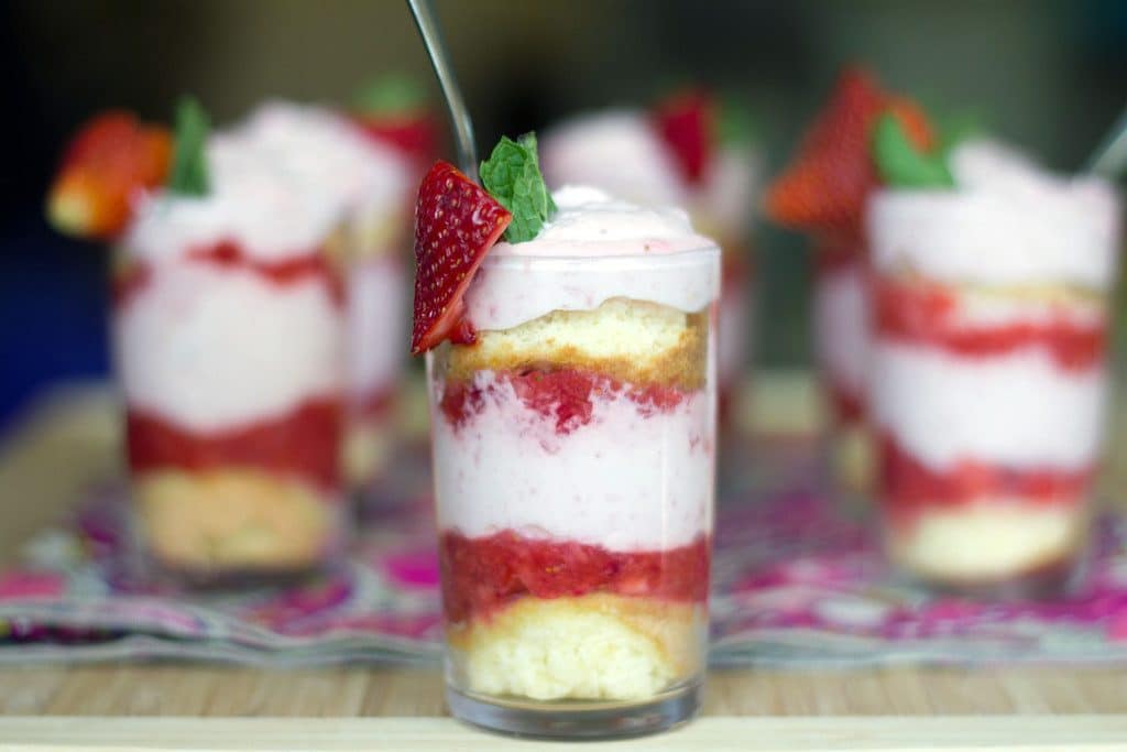 Landscape head-on view of a strawberry mousse parfait with layers of sponge cake, strawberry purée, and strawberry mousse with more parfaits in the background