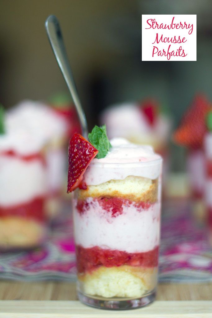 Head-on view of a mini strawberry mousse parfait with sponge cake, strawberry purée and strawberry mousse with more parfaits in background and recipe title at top